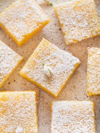 Close up overhead shot of a Meyer lemon bar garnished with powdered sugar and a tiny white edible flower.