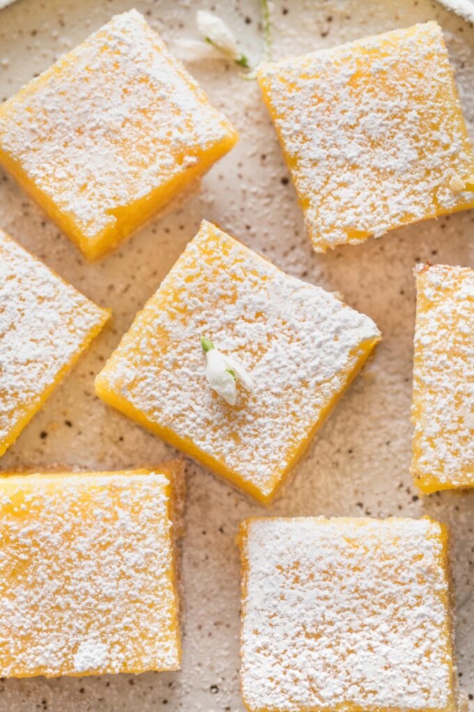 Close up overhead shot of a Meyer lemon bar garnished with powdered sugar and a tiny white edible flower.