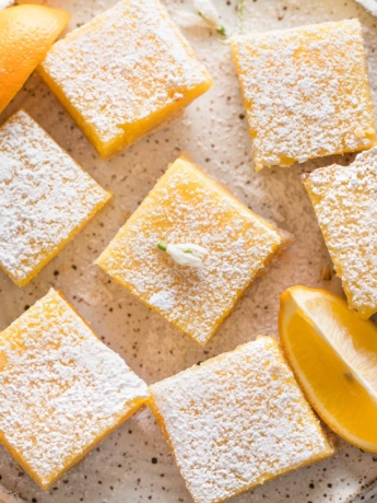 Close up overhead image of Meyer lemon bars on a plate with lemon slices and dusted powdered sugar.