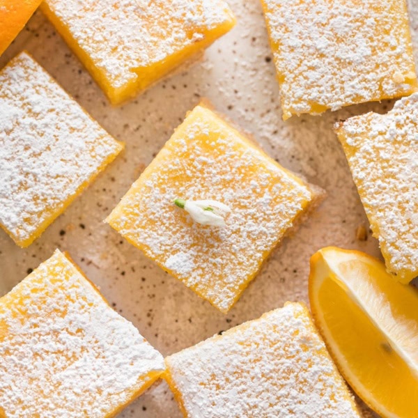 Close up overhead image of Meyer lemon bars on a plate with lemon slices and dusted powdered sugar.