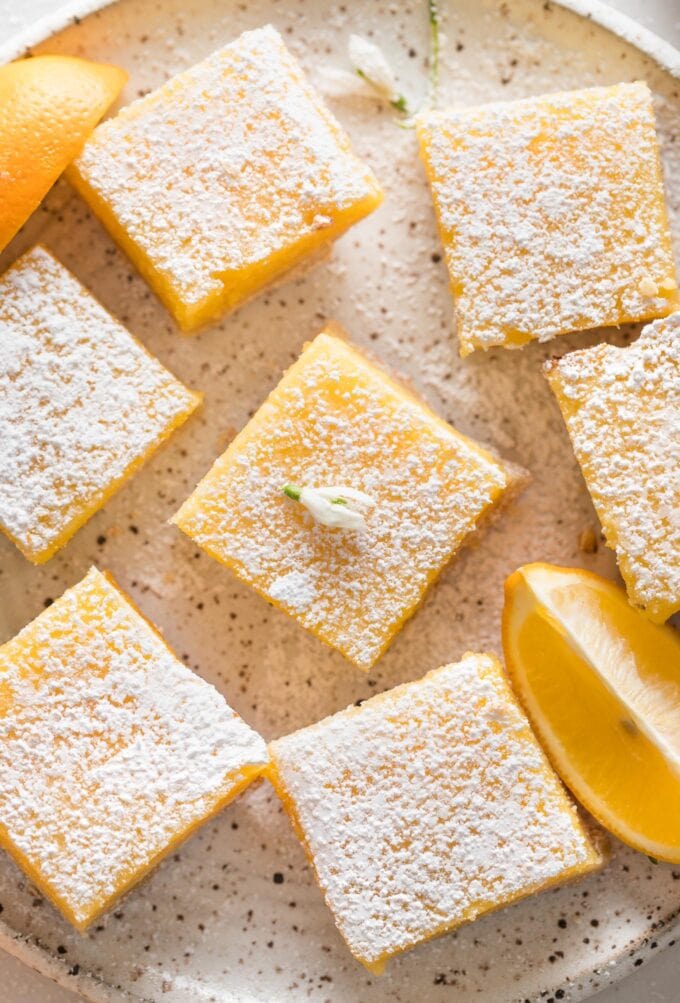Close up overhead image of Meyer lemon bars on a plate with lemon slices and dusted powdered sugar.