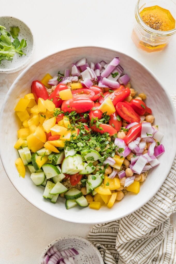 Chopped pepper, onion, tomatoes, parsley, and cucumber added to bowl with quinoa.