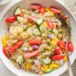 Bowl full of quinoa chickpea salad with tomatoes, cucumber, and a lemon dressing.