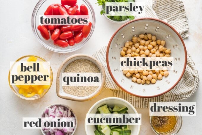 Labeled photo of cherry tomatoes, chickpeas, fresh parsley, uncooked quinoa, bell pepper, red onion, cucumber, and a lemon dressing in prep bowls and jars.