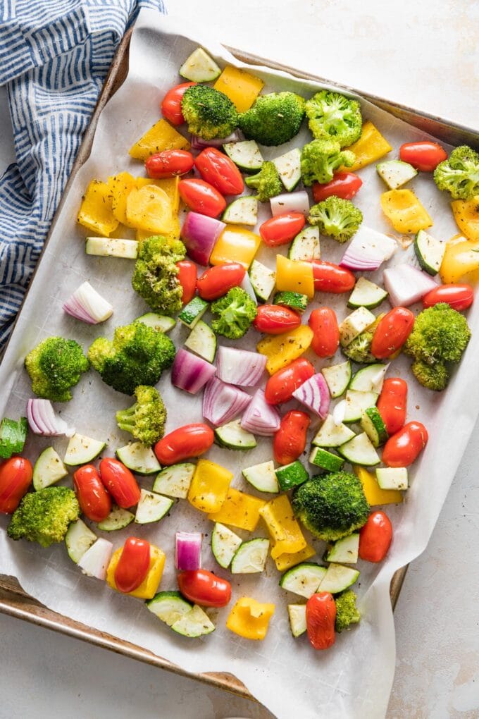 Rimmed sheet pan filled with seasoned vegetables ready to roast.
