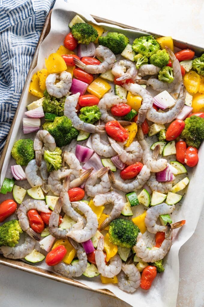 Sheet pan with partly roasted vegetables and raw shrimp ready to cook for a simple sheet pan dinner.