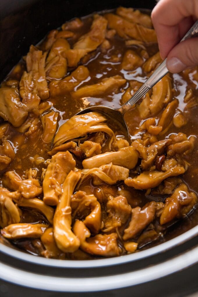 Shredded teriyaki chicken being scooped out of the bowl of a Crockpot.