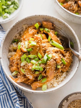 Bowl full of slow cooker teriyaki chicken served over rice with green onions and sesame seeds.