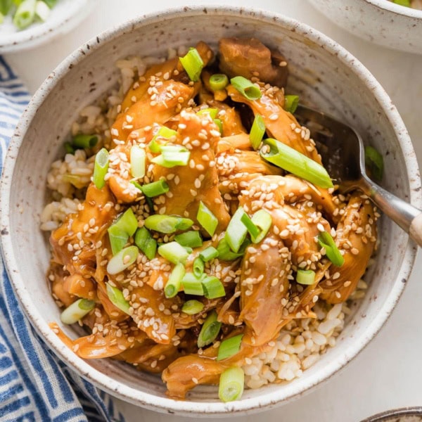 Bowl full of slow cooker teriyaki chicken served over rice with green onions and sesame seeds.