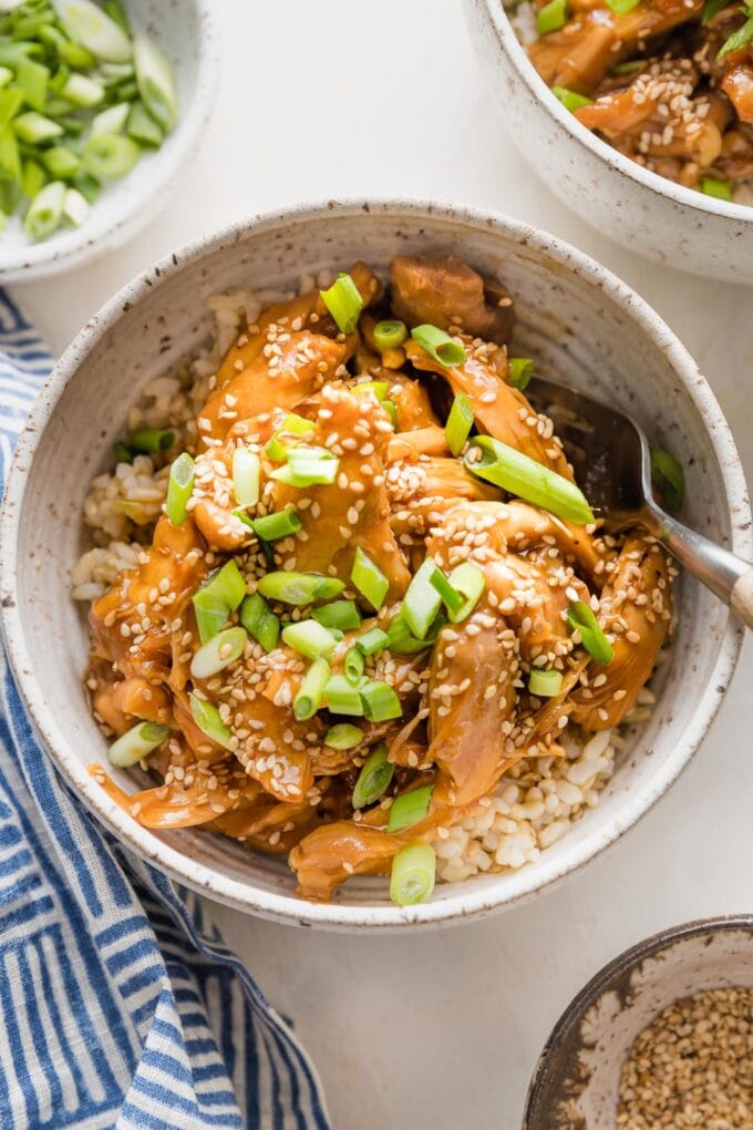 Bowl full of slow cooker teriyaki chicken served over rice with green onions and sesame seeds.