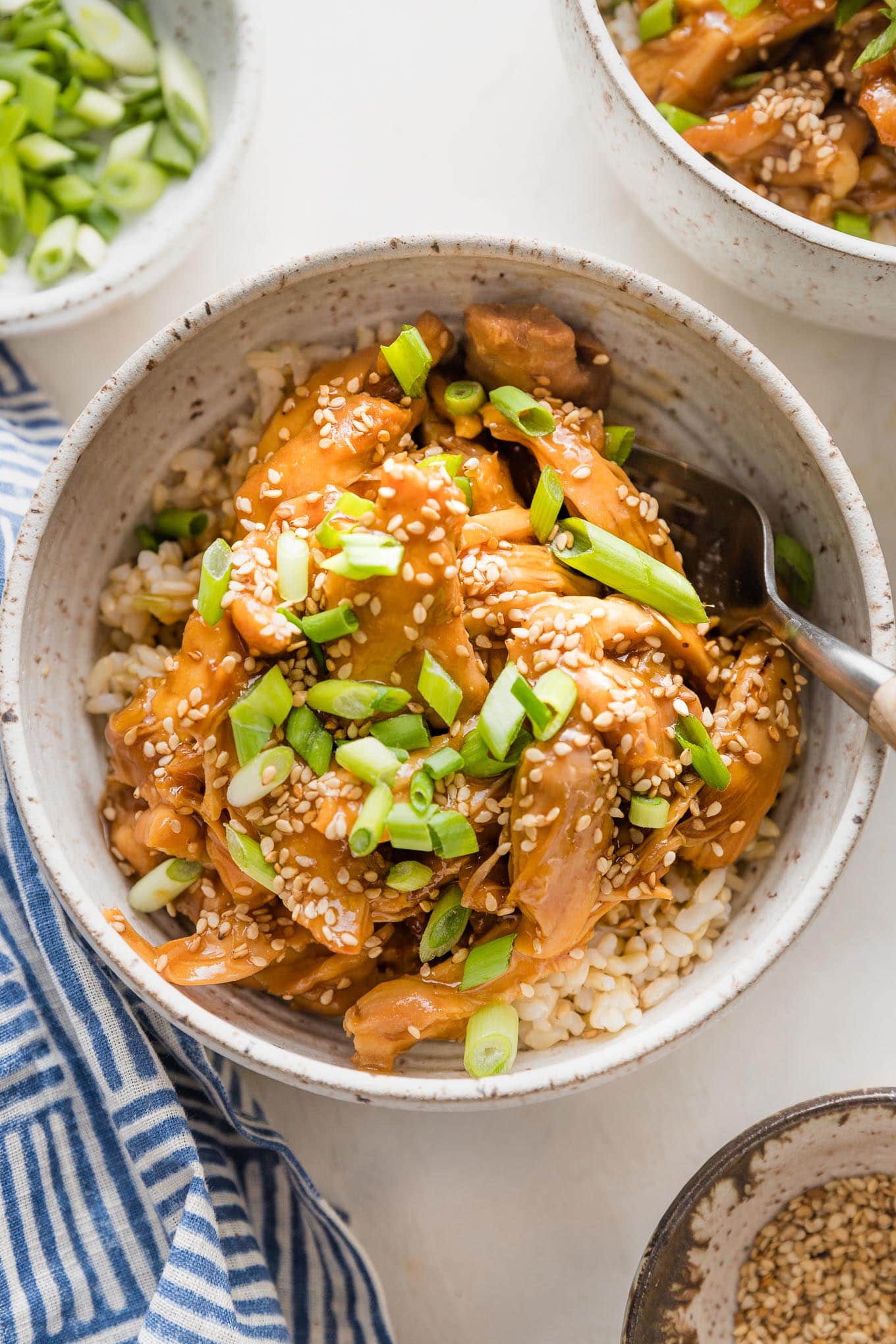 Bowl full of slow cooker teriyaki chicken served over rice with green onions and sesame seeds.