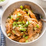 Close up of teriyaki chicken in a bowl with rice, sesame seeds, and green onions.