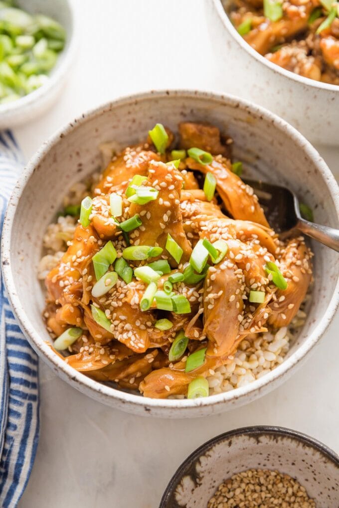 Close up of teriyaki chicken in a bowl with rice, sesame seeds, and green onions.