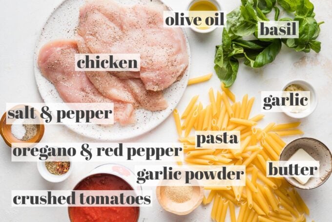 Labeled photo of chicken breasts, pasta, crushed tomatoes, minced garlic, fresh basil, butter, olive oil, and seasonings in prep bowls ready to cook.