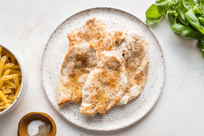 Pan-fried chicken breasts resting on a small white plate.