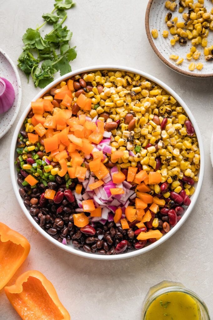 White bowl holding corn, beans, jalapeno pepper, and chopped orange bell pepper.