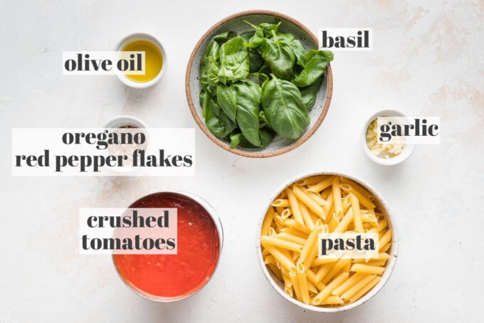 Labeled photo of pasta, crushed tomatoes, fresh basil leaves, minced garlic, olive oil, dried oregano, and red pepper flakes arranged and measured out into prep bowls.