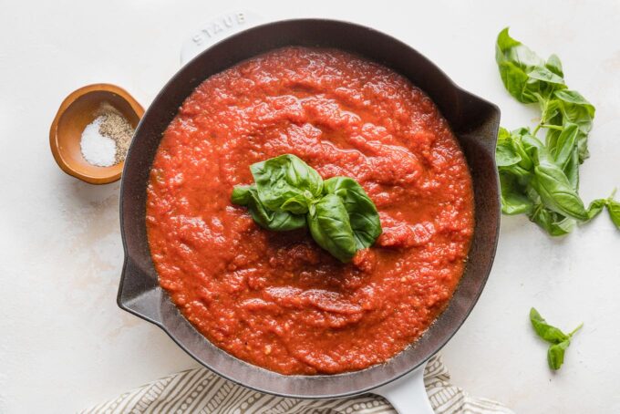 Homemade marinara sauce with fresh basil sprigs in a skillet.