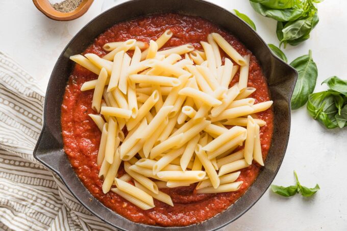 Al dente penne pasta added to a skillet with homemade marinara sauce.