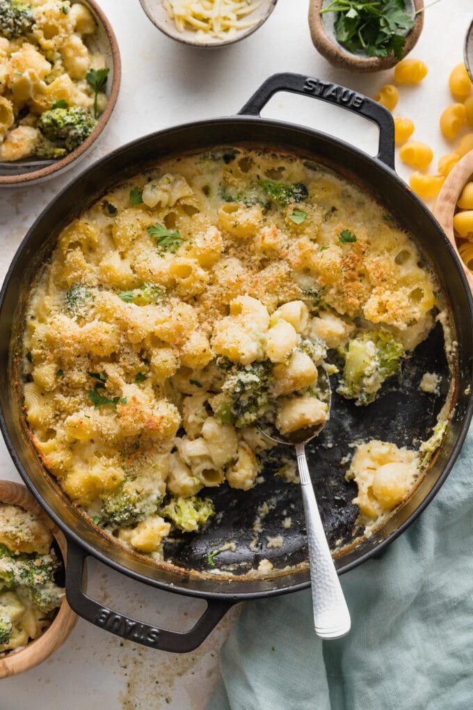 Large cast iron pan half full of baked broccoli mac and cheese.