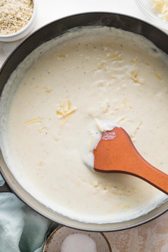 Shredded cheese melting into bechamel sauce as it is stirred.