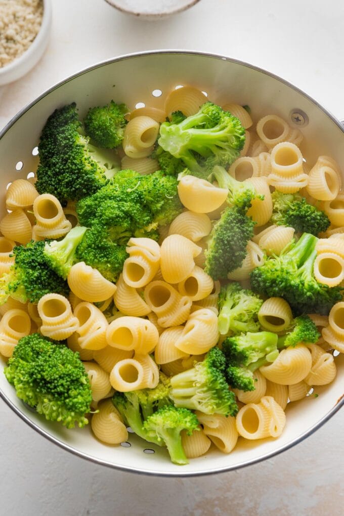 Cooked pasta and broccoli together in a beige colander.