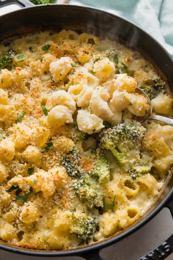 A serving spoon dishing out a helping of baked broccoli mac and cheese.