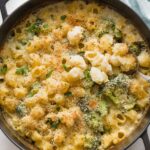 Large cast iron pan full of baked broccoli mac and cheese with a serving spoon lifting out a portion.