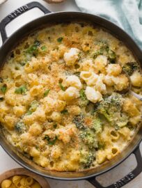 Large cast iron pan full of baked broccoli mac and cheese with a serving spoon lifting out a portion.