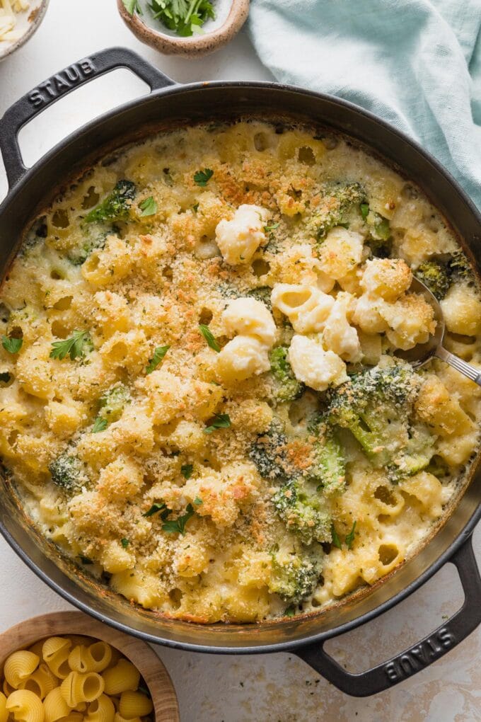 Large cast iron pan full of baked broccoli mac and cheese with a serving spoon lifting out a portion.