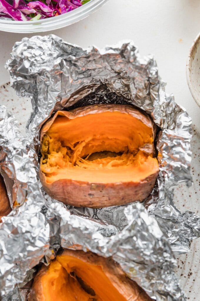 Close up of a baked sweet potato wrapped in foil and sliced open to reveal the tender interior.