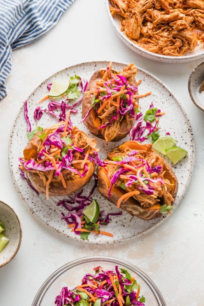 Overhead image of a white ceramic plate with three BBQ chicken stuffed sweet potatoes topped with sunset slaw.