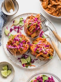 White plate with BBQ chicken stuffed sweet potatoes topped with sunset slaw.