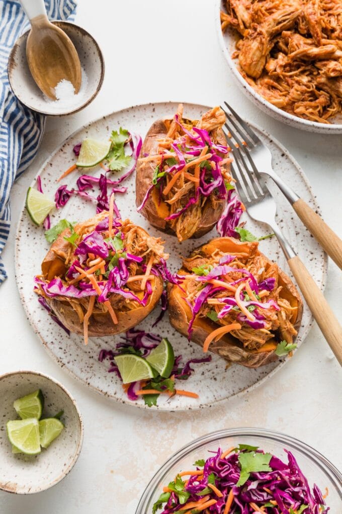 White plate with BBQ chicken stuffed sweet potatoes topped with sunset slaw.