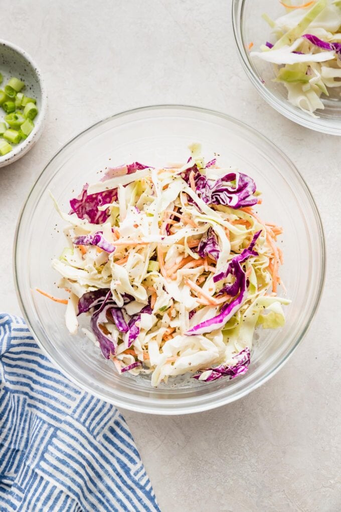 Shredded white cabbage, red cabbage, and carrots in a clear bowl.