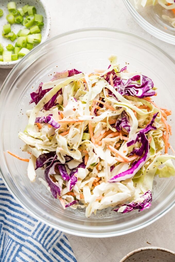 Close up of homemade healthy coleslaw with red and white cabbage, carrots, green onions, and a light dressing in a clear serving bowl.