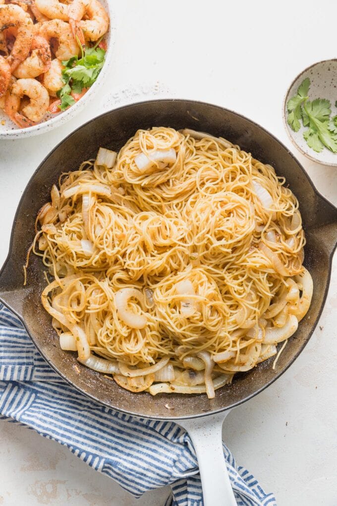 Pasta and seasonings added to onion in a skillet.