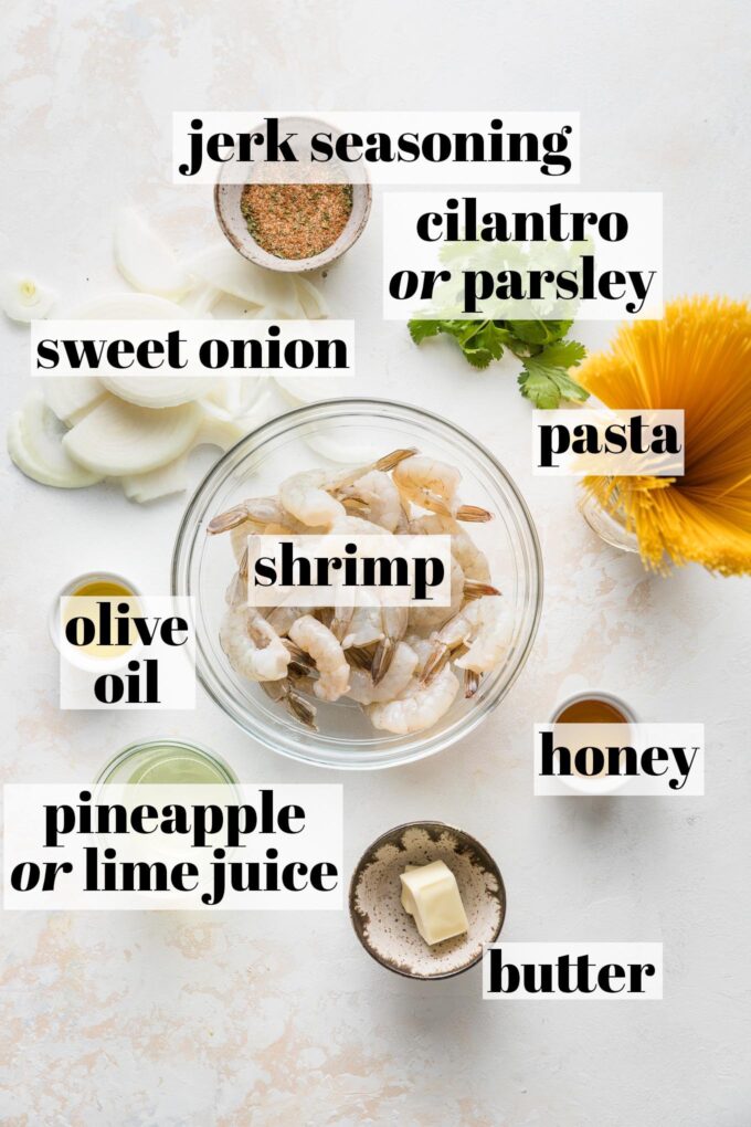 Overhead image of prep bowls holding raw shrimp, uncooked angel hair pasta, jerk seasoning, parsley, sweet onion, olive oil, honey, butter, and pineapple juice.