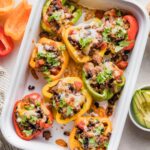White ceramic casserole dish filled with taco stuffed peppers with melted cheese and cilantro on top.