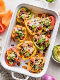 White ceramic casserole dish filled with taco stuffed peppers with melted cheese and cilantro on top.