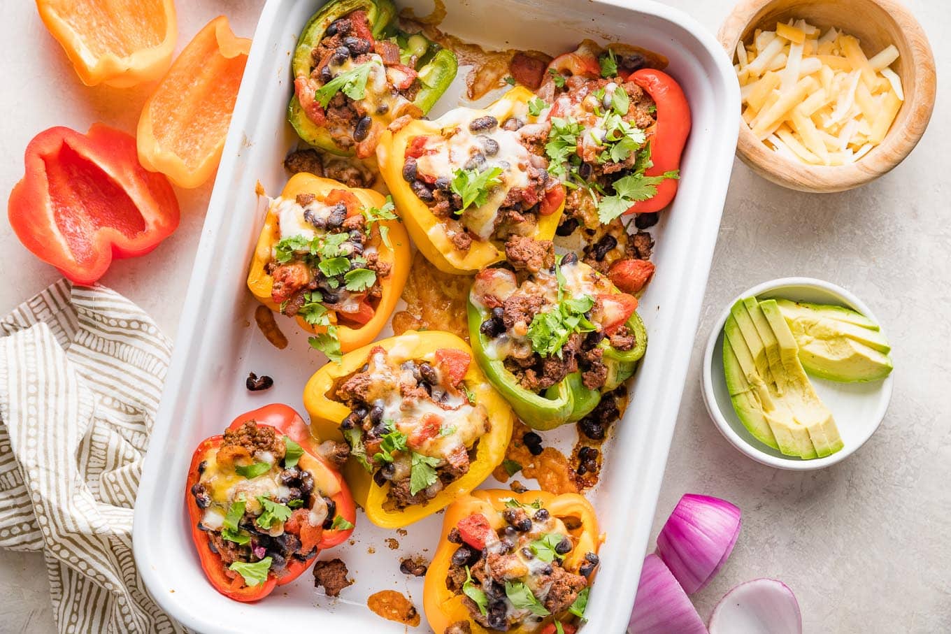 White ceramic casserole dish filled with taco stuffed peppers with melted cheese and cilantro on top.