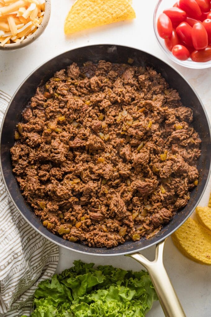 Saute pan filled with a taco filling of cooked ground beef, taco seasoning, salt, and green chilies.