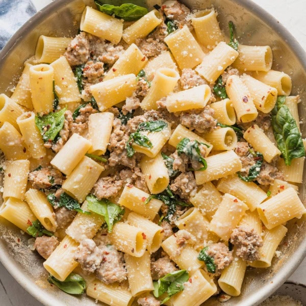 A skillet full of creamy Italian sausage pasta with baby spinach and Parmesan.