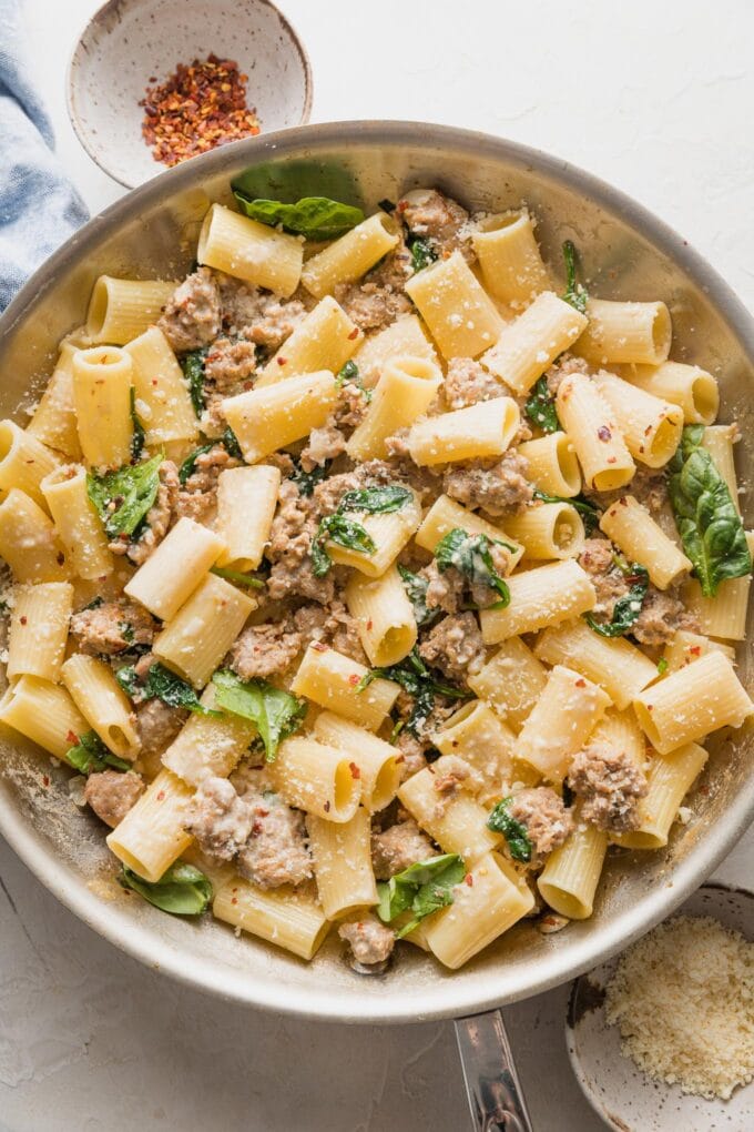 A skillet full of creamy Italian sausage pasta with baby spinach and Parmesan.
