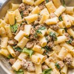Close-up of a skillet full of creamy Italian sausage pasta with baby spinach and Parmesan.