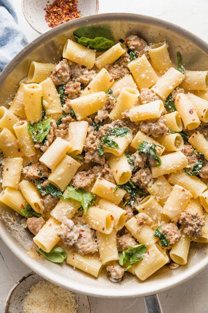 Close-up of a skillet full of creamy Italian sausage pasta with baby spinach and Parmesan.