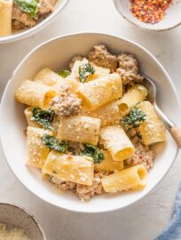 Small bowl filled with a generous serving of creamy Italian sausage pasta with red pepper flakes and grated Parmesan cheese.