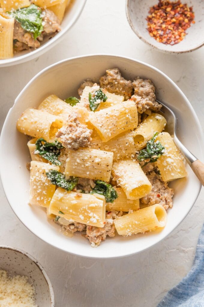 Small bowl filled with a generous serving of creamy Italian sausage pasta with red pepper flakes and grated Parmesan cheese.