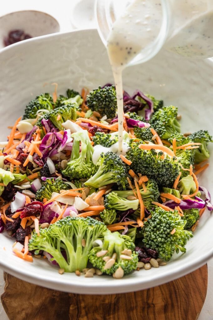 Close up of a creamy salad dressing being poured on top of a broccoli salad.