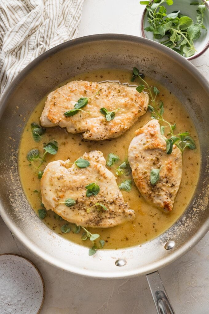 Overhead image of oregano chicken in a skillet with fresh oregano sprigs scattered around.